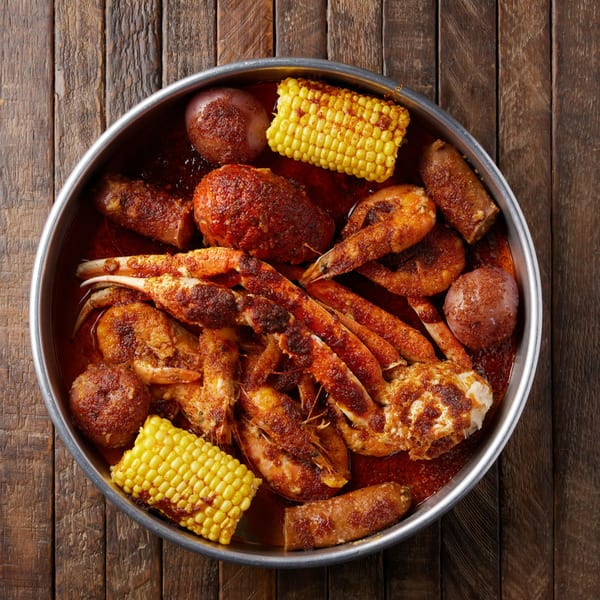 A Crab N Spice seafood boil with crab legs, shrimp, sausage, corn, and potatoes in a metal pan.