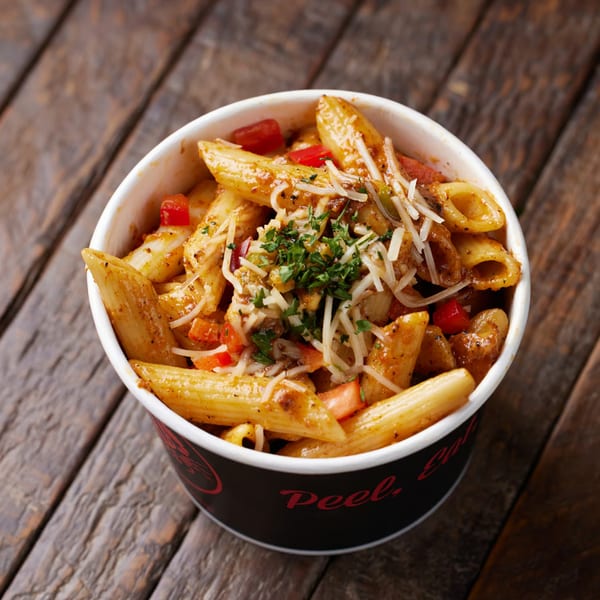 Penne pasta with sauce, red peppers, shredded cheese, and parsley in a black and white cup.