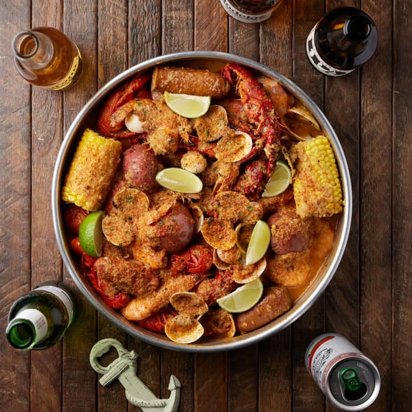 A large metal platter of Crab N Spice seafood boil with crawfish, shrimp, clams, corn, and potatoes.