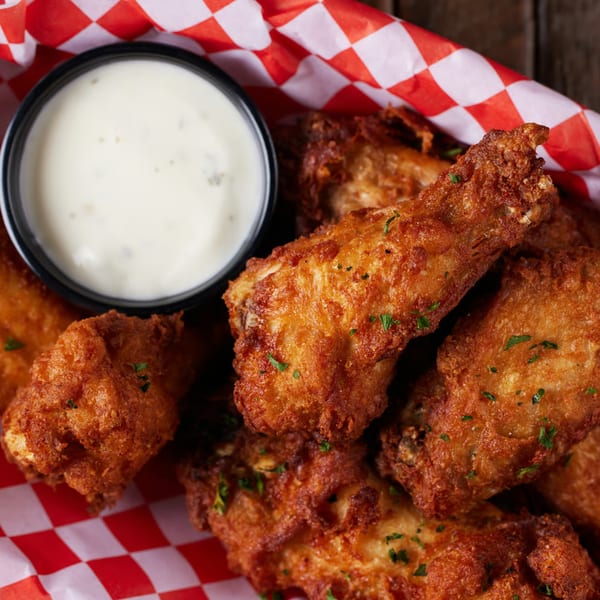 Crispy fried chicken wings with parsley flakes, served with a side of creamy ranch dressing.