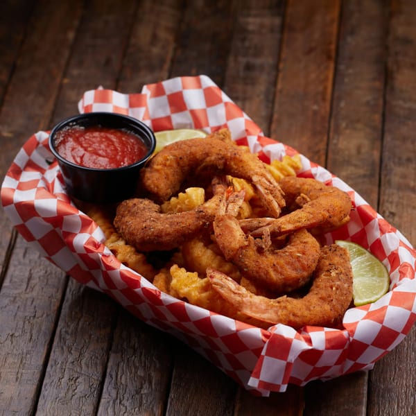 Crispy fried shrimp and crinkle-cut fries in a red and white checkered basket with ketchup and lime.